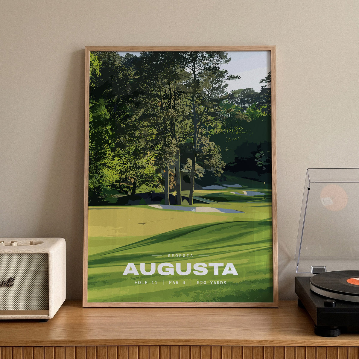 Augusta 11th hole golf print of a green below tall Georgia pines, framed on a sideboard beside a record player