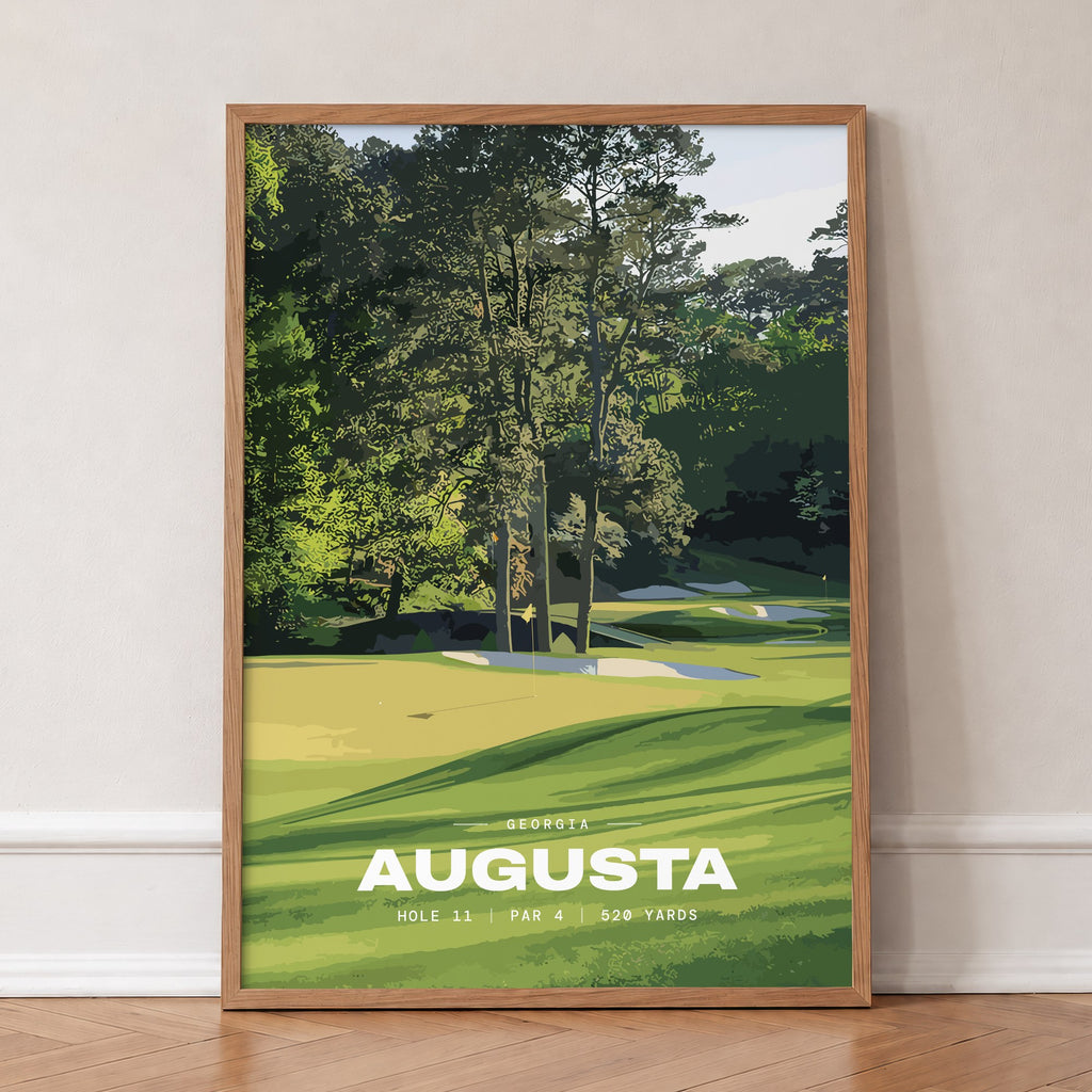 Augusta 11th hole golf print of a green below tall Georgia pines, in an oak frame, leaning against a wall on a herringbone floor