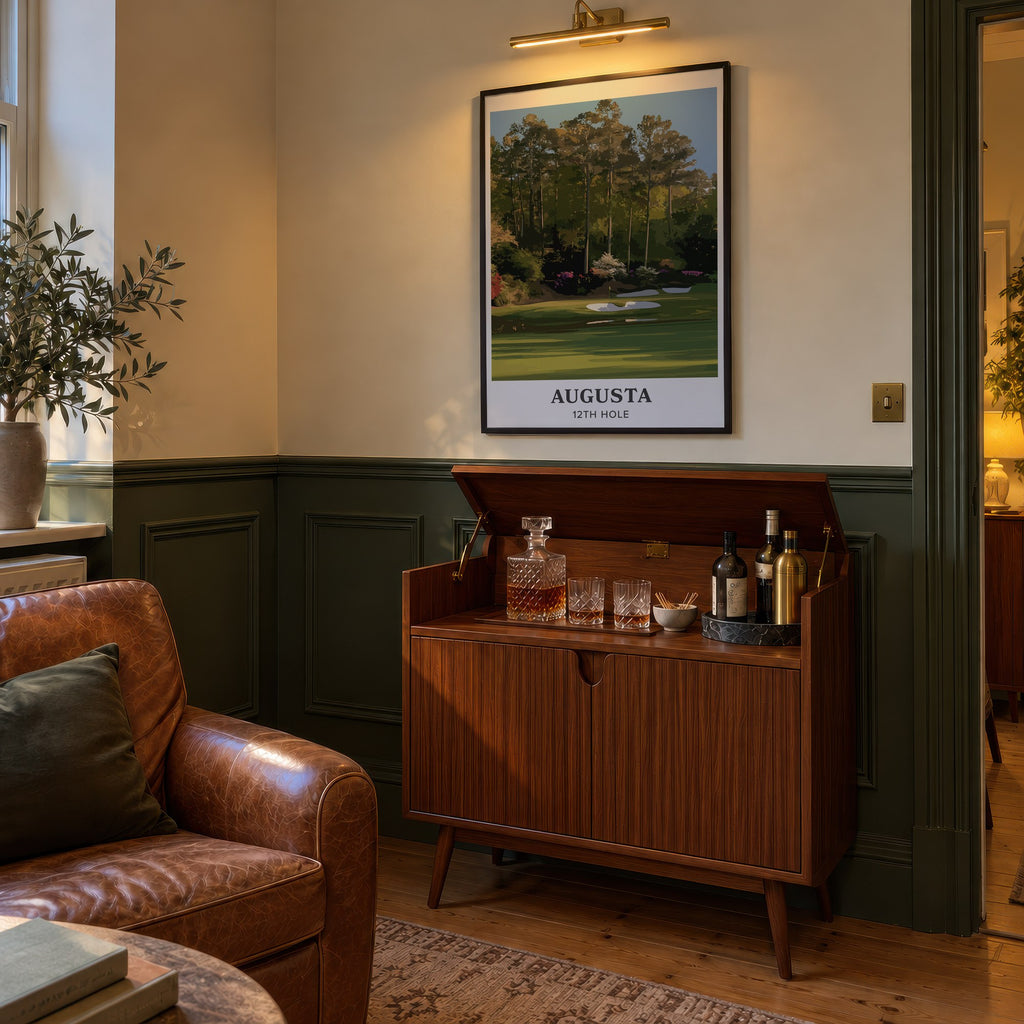 Augusta 12th hole golf print of a par 3 green below azaleas, cream border, framed above a bar cabinet beside a leather armchair