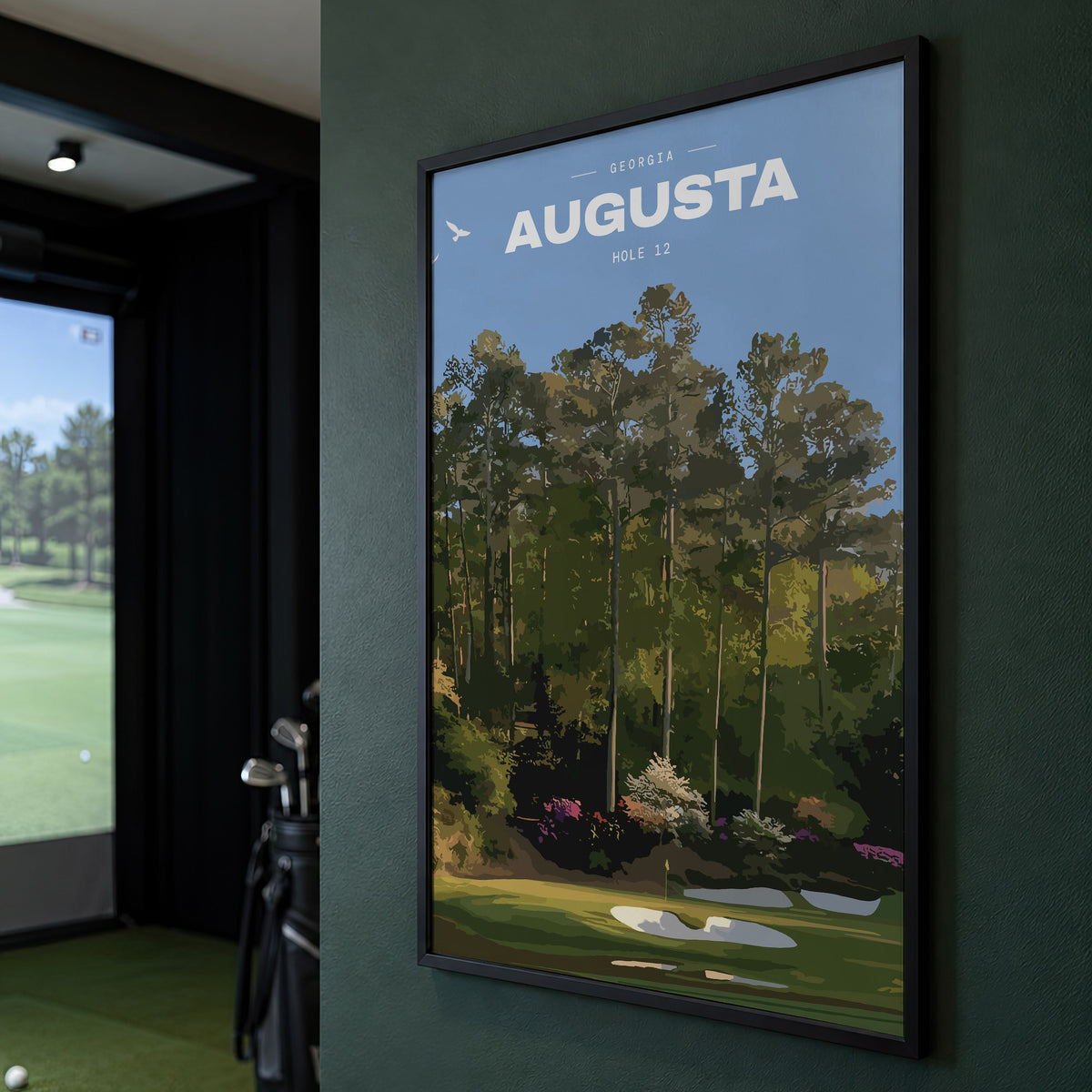 Augusta 12th hole golf print of a par 3 green below azaleas and pines, framed on a green wall beside a golf simulator