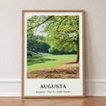 Augusta 13th hole golf print of a par 5 fairway under oak and pines, in an oak frame, leaning against a wall on a herringbone floor