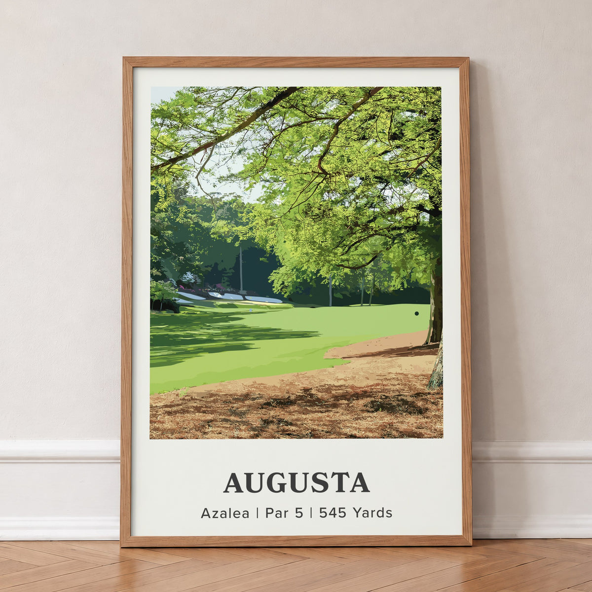 Augusta 13th hole golf print of a par 5 fairway under oak and pines, in an oak frame, leaning against a wall on a herringbone floor