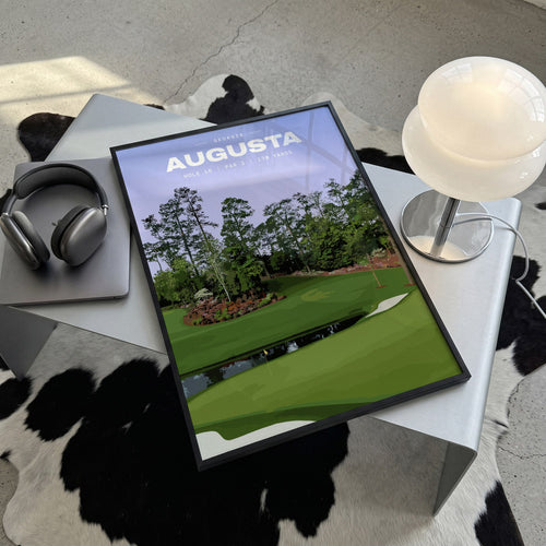 Augusta 16th hole golf print of a par 3 green across water, azaleas behind, framed, lying on a steel table on a cowhide rug