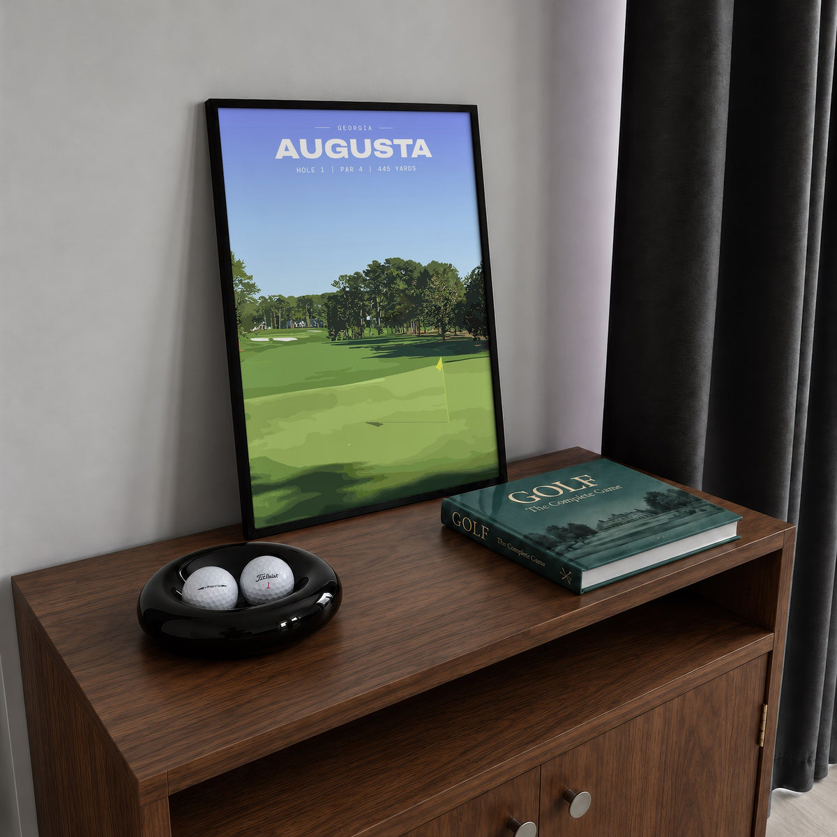 Augusta 1st hole golf print of an uphill fairway to a yellow flag, framed on a walnut cabinet beside golf balls and a golf book