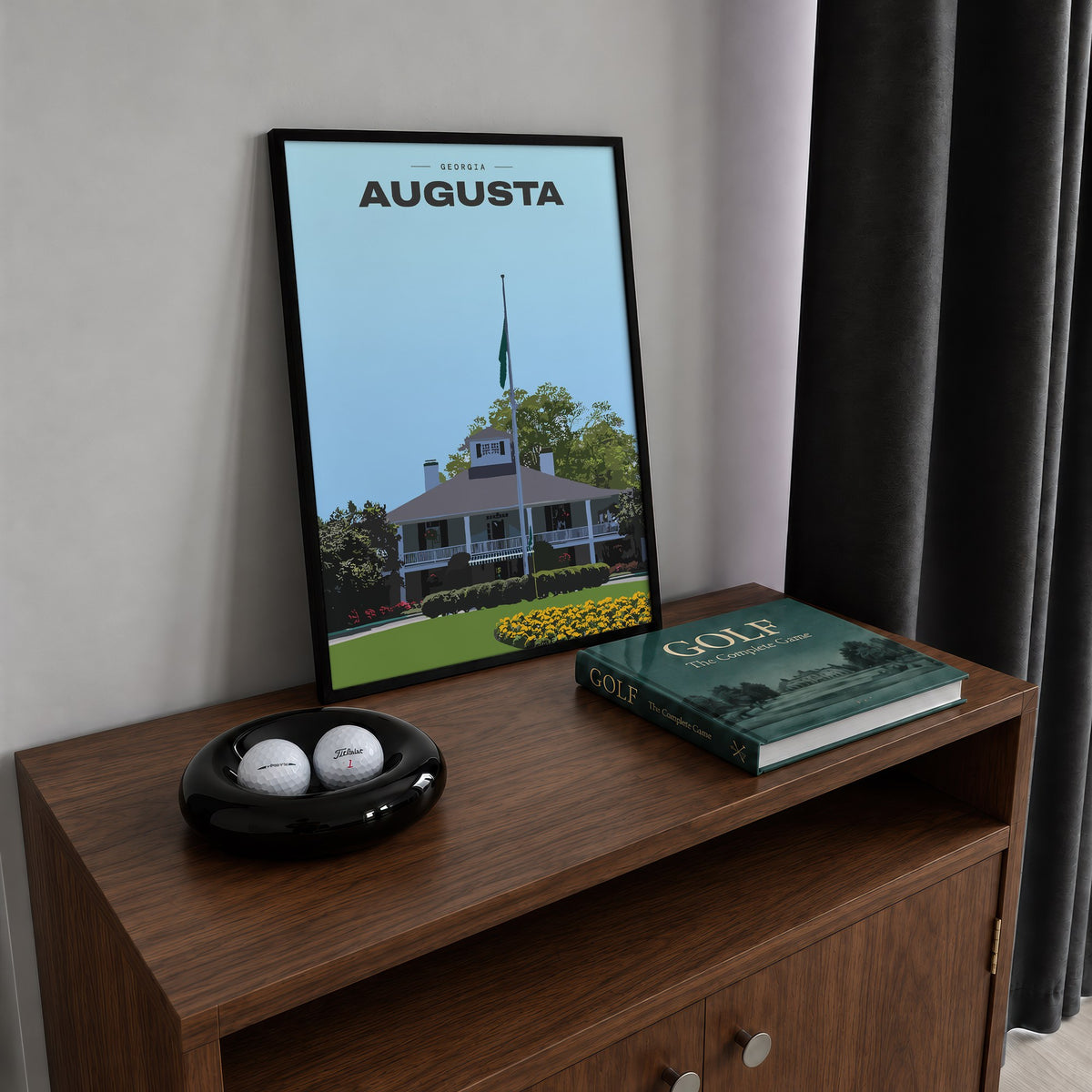 Augusta The Clubhouse golf print of the white clubhouse and yellow flowers, framed on a walnut cabinet beside golf balls and a golf book