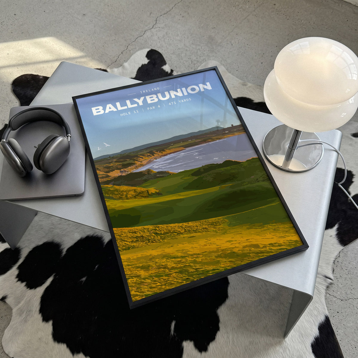 Ballybunion 11th hole golf print of dunes running down to an Atlantic bay, framed, lying on a steel table on a cowhide rug