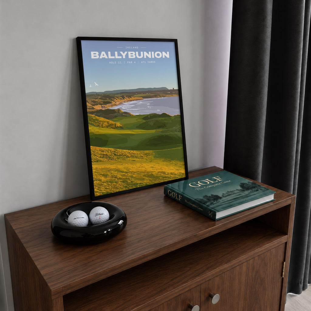 Ballybunion 11th hole golf print of dunes running down to an Atlantic bay, framed on a walnut cabinet beside golf balls and a golf book