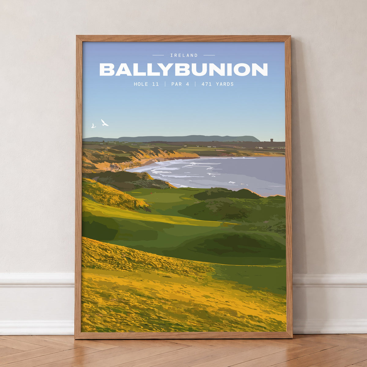 Ballybunion 11th hole golf print of dunes running down to an Atlantic bay, in an oak frame, leaning against a wall on a herringbone floor