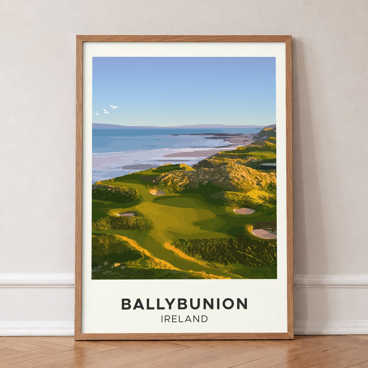Ballybunion golf print of links greens above the sea, cream border, in an oak frame, leaning against a wall on a herringbone floor