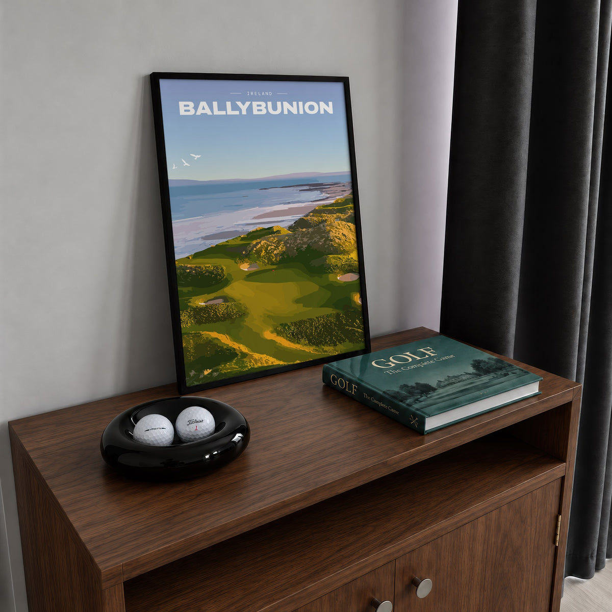 Ballybunion golf print of links greens in the dunes above the sea, framed on a walnut cabinet beside golf balls and a golf book