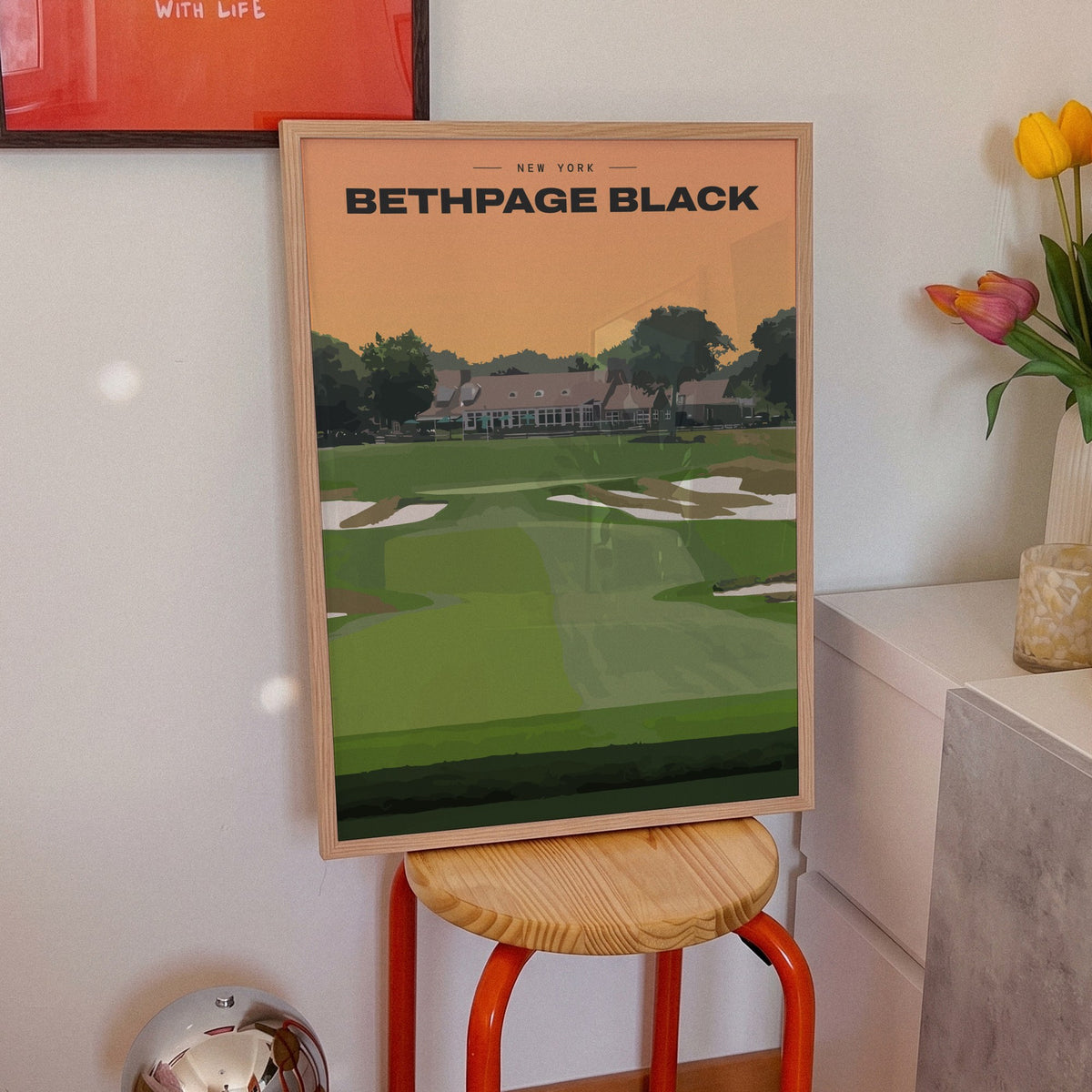Bethpage Black golf print of a bunkered fairway up to the clubhouse, framed on an orange stool beside tulips