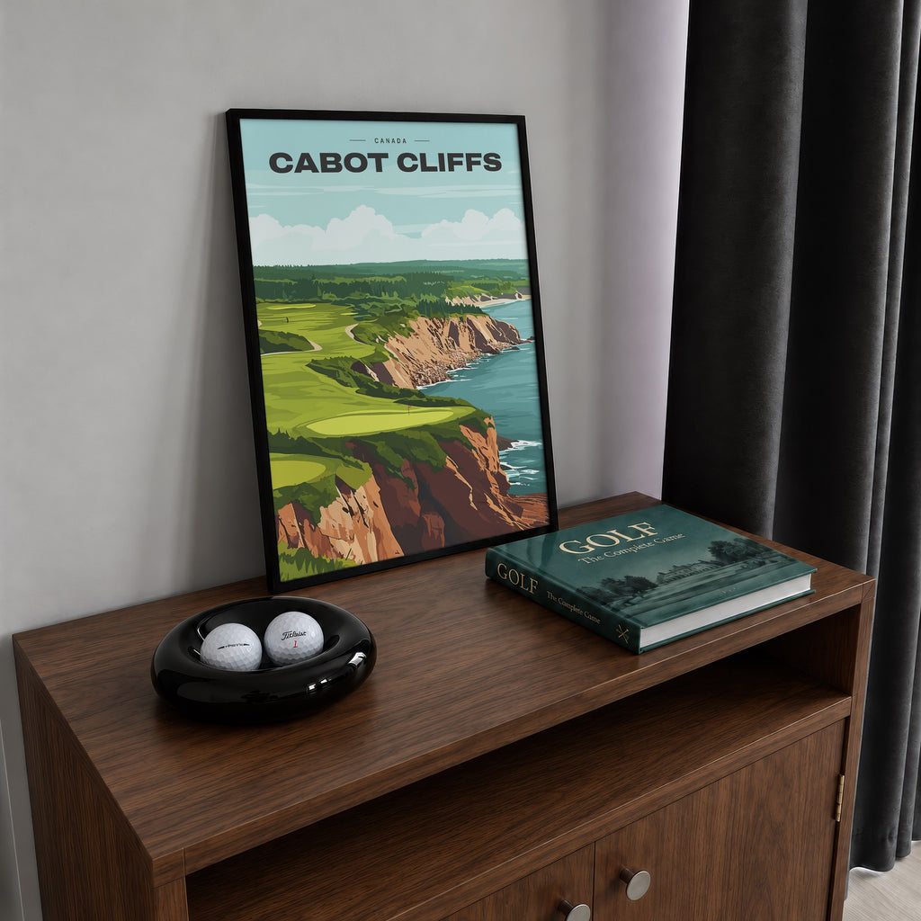 Cabot Cliffs golf print of a green on red clifftops above the sea, framed on a walnut cabinet beside golf balls and a golf book