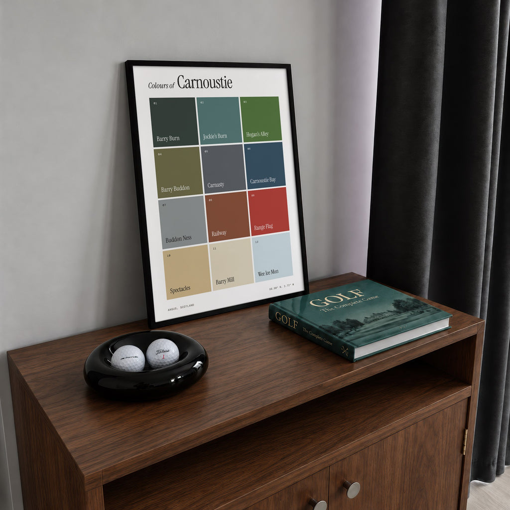 Colours of Carnoustie print of twelve named colour squares on white, framed on a walnut cabinet beside golf balls and a golf book