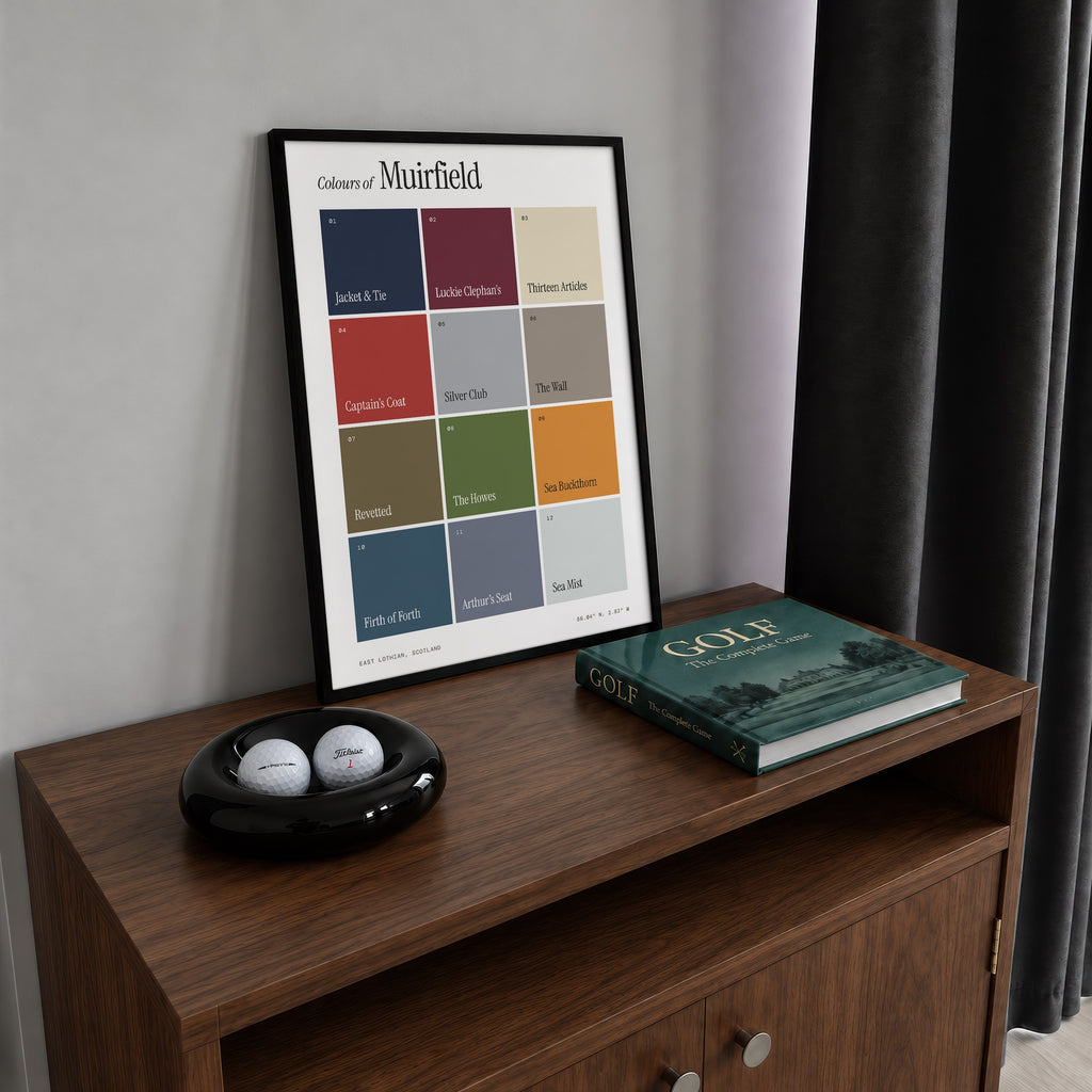 Colours of Muirfield print of twelve named colour squares on white, framed on a walnut cabinet beside golf balls and a golf book