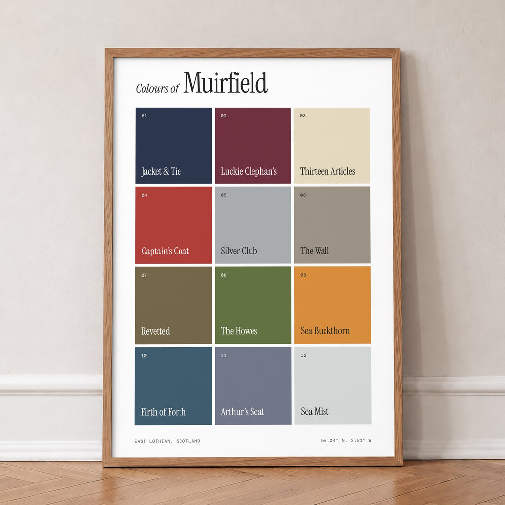 Colours of Muirfield print of twelve named colour squares on white, in an oak frame, leaning against a wall on a herringbone floor