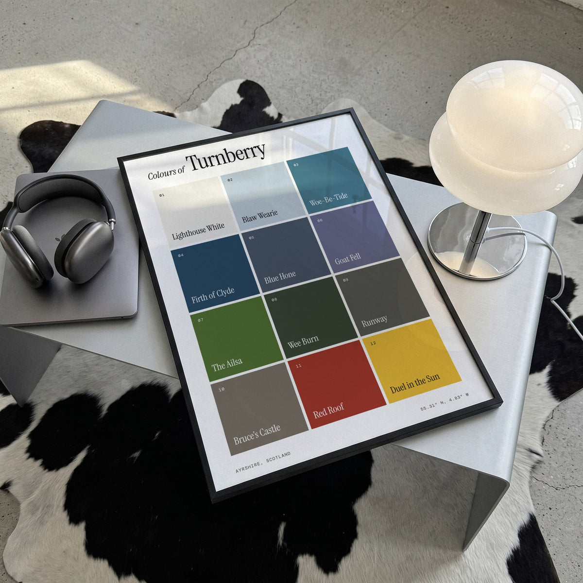 Colours of Turnberry print of twelve named colour squares on white, framed, lying on a steel table on a cowhide rug