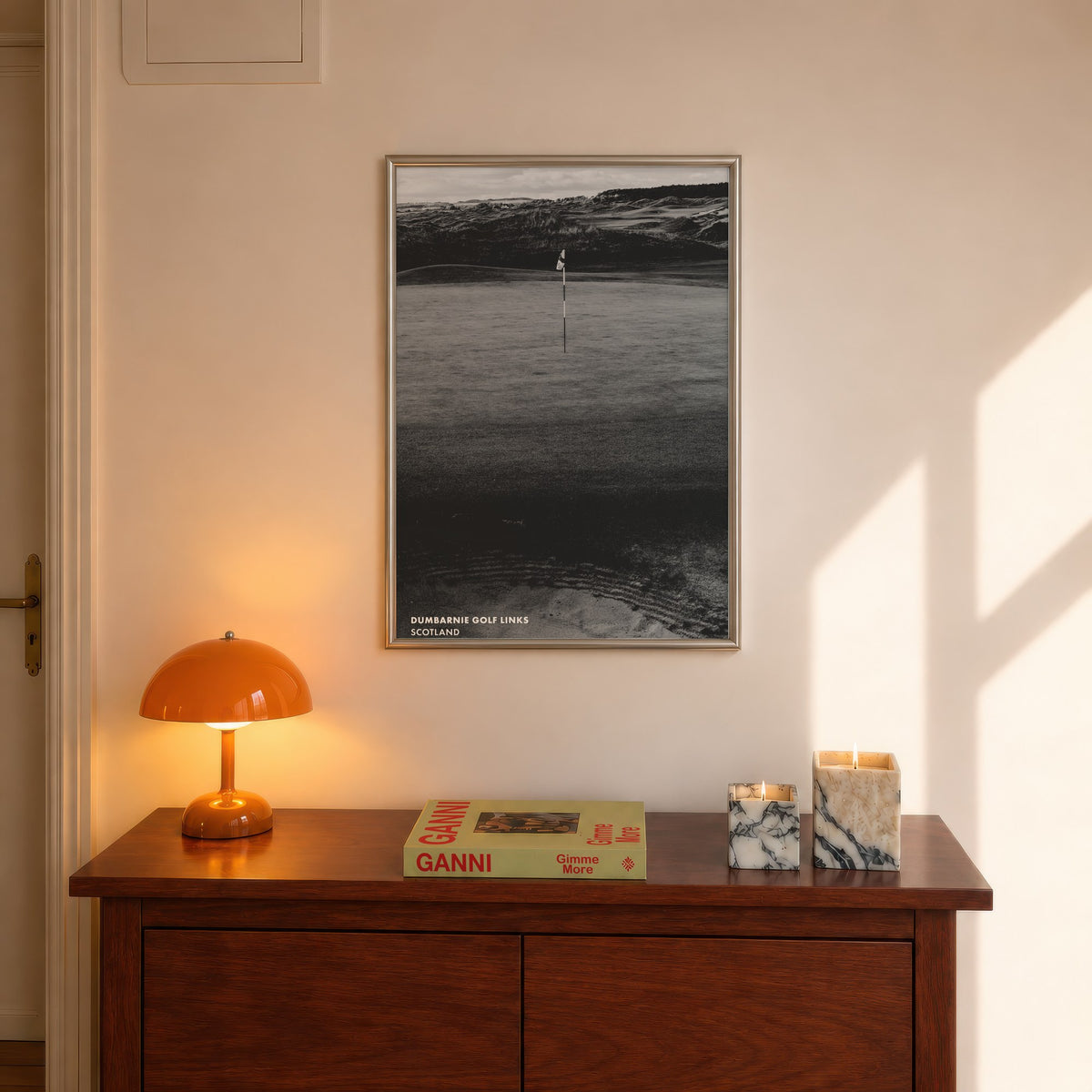 Dumbarnie golf print of a black and white photo of a flag below dunes, framed above a console beside an orange lamp