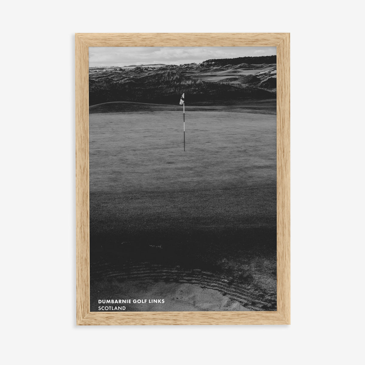 Dumbarnie golf print of a black and white photo of a flag below dunes, in a natural wood frame on a plain wall