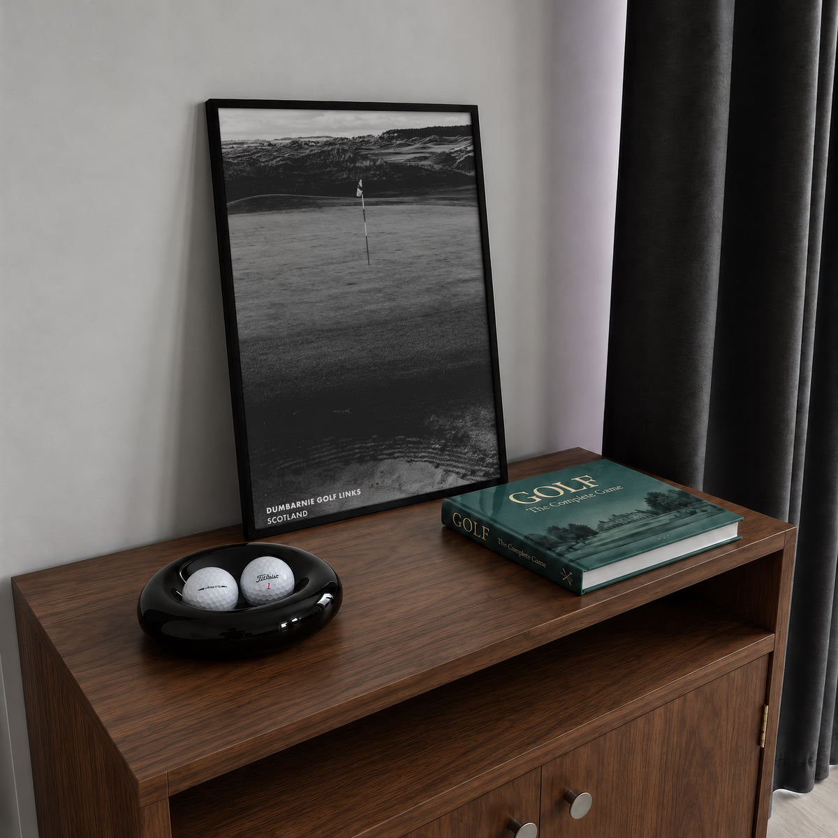 Dumbarnie golf print of a black and white photo of a flag below dunes, framed on a walnut cabinet beside golf balls and a golf book