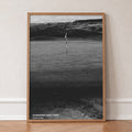 Dumbarnie golf print of a black and white photo of a flag below dunes, in an oak frame, leaning against a wall on a herringbone floor