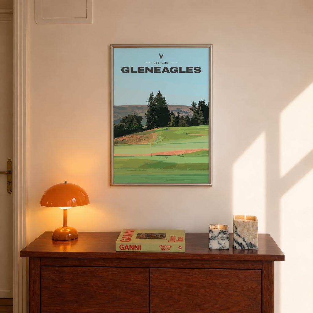 Gleneagles golf print of a green below pines and Perthshire hills, framed above a console beside an orange lamp