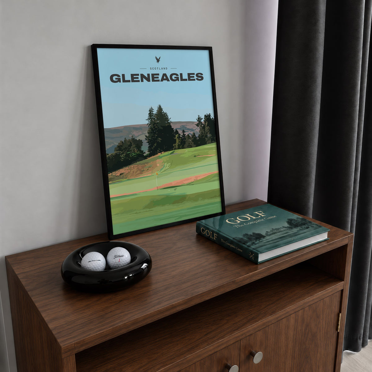Gleneagles golf print of a green below pines and Perthshire hills, framed on a walnut cabinet beside golf balls and a golf book
