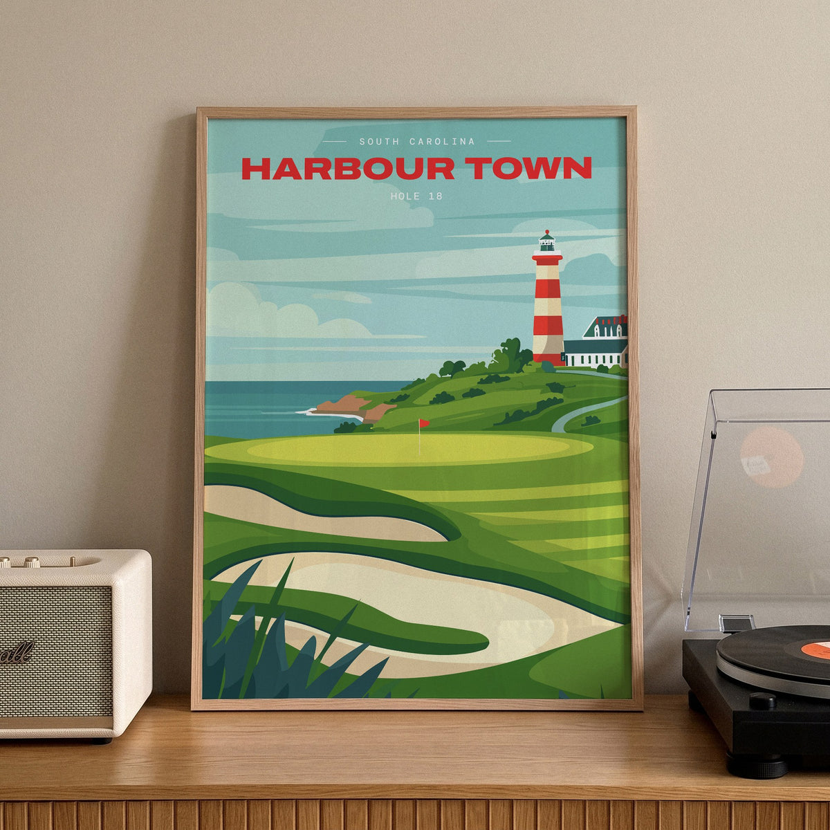 Harbour Town 18th hole golf print of a green below a striped lighthouse, framed on a sideboard beside a record player