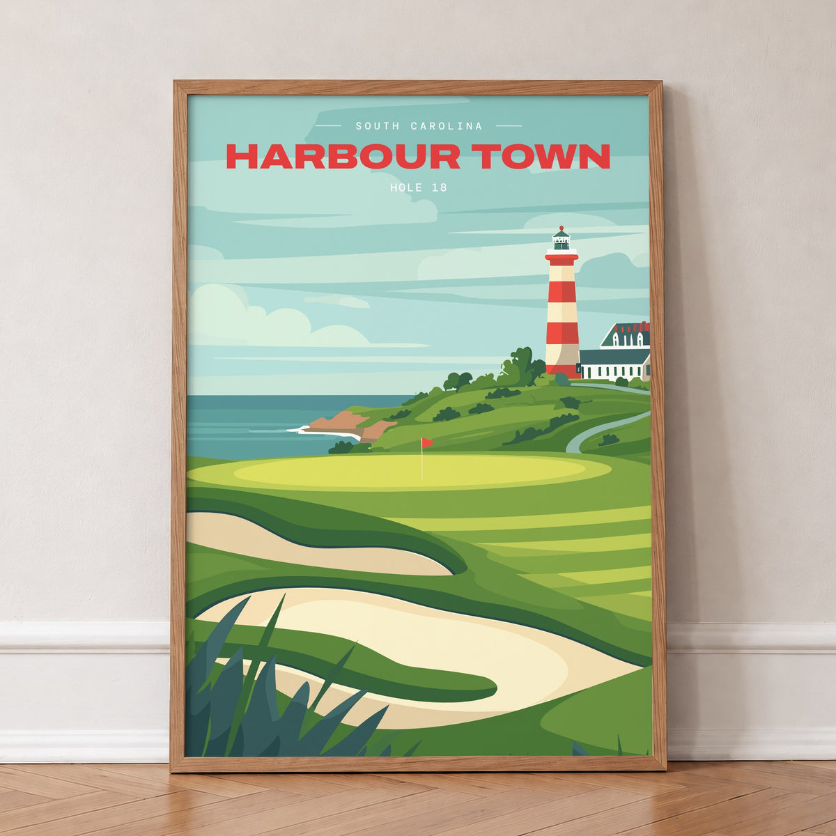 Harbour Town 18th hole golf print of a green below a striped lighthouse, in an oak frame, leaning against a wall on a herringbone floor