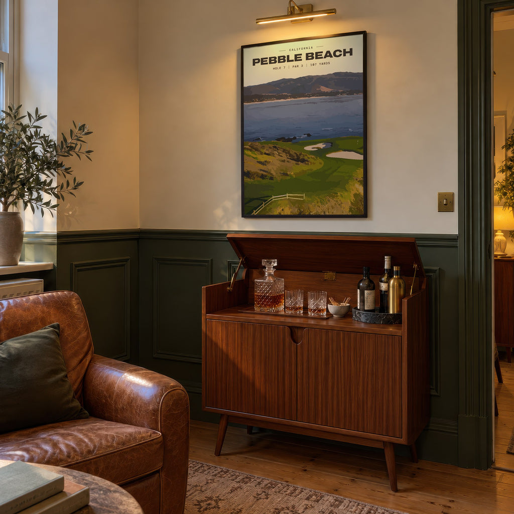 Pebble Beach 7th hole golf print of a small green on a point above the bay, framed above a bar cabinet beside a leather armchair