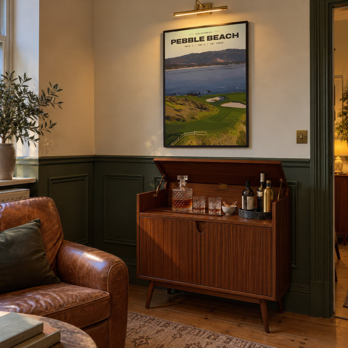 Pebble Beach 7th hole golf print of a small green on a point above the bay, framed above a bar cabinet beside a leather armchair