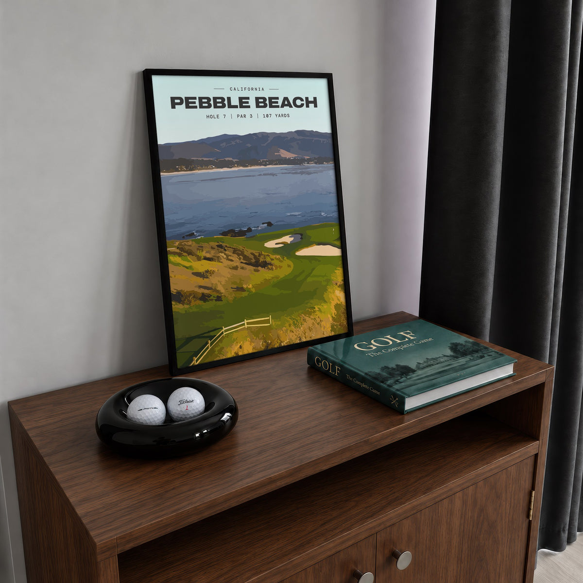 Pebble Beach 7th hole golf print of a small green on a point above the bay, framed on a walnut cabinet beside golf balls and a golf book