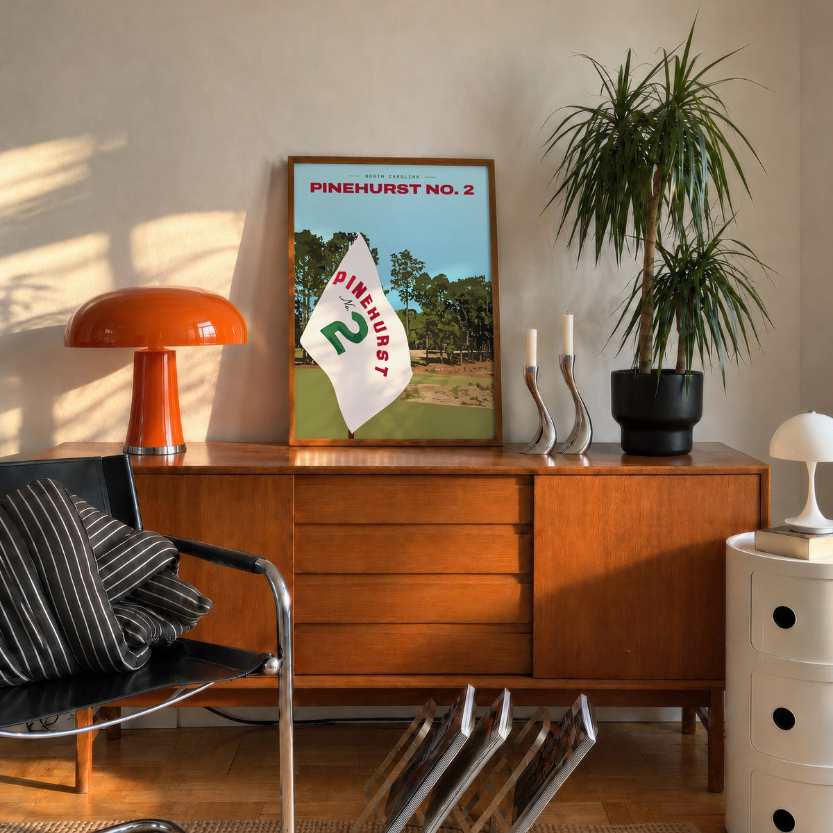 Pinehurst No. 2 golf print of a white pin flag before sandy waste and pines, framed on a mid-century sideboard beside an orange lamp
