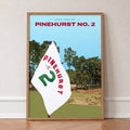 Pinehurst No. 2 golf print of a white pin flag before sandy waste and pines, in an oak frame, leaning against a wall on a herringbone floor