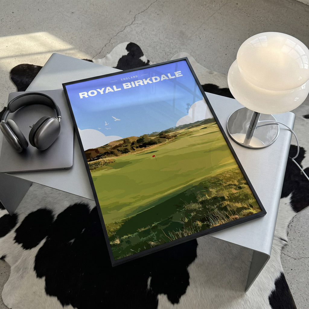 Royal Birkdale golf print of a links fairway and red flag between dunes, framed, lying on a steel table on a cowhide rug