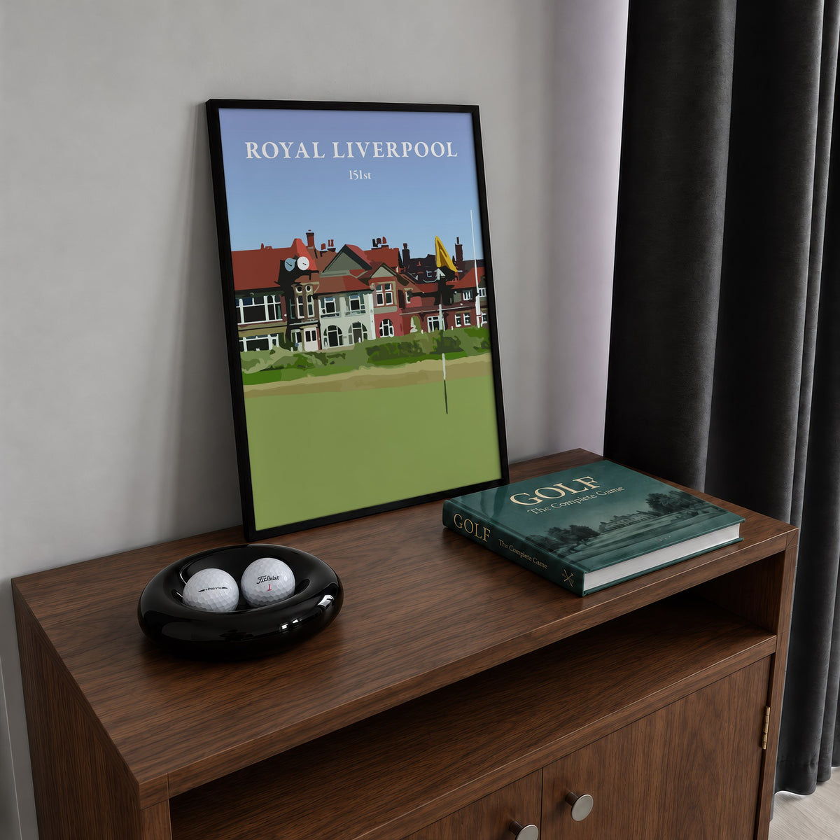 Royal Liverpool 2023 golf print of the clubhouse behind a yellow flag, framed on a walnut cabinet beside golf balls and a golf book