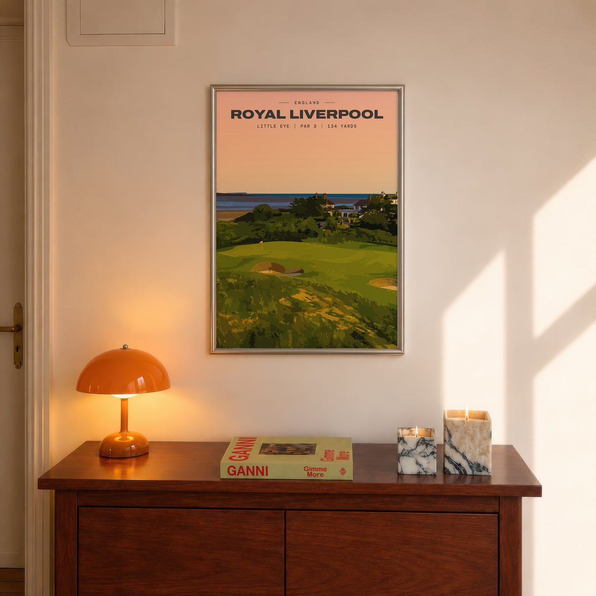 Royal Liverpool Little Eye golf print of a raised par 3 green at sunset, framed above a console beside an orange lamp