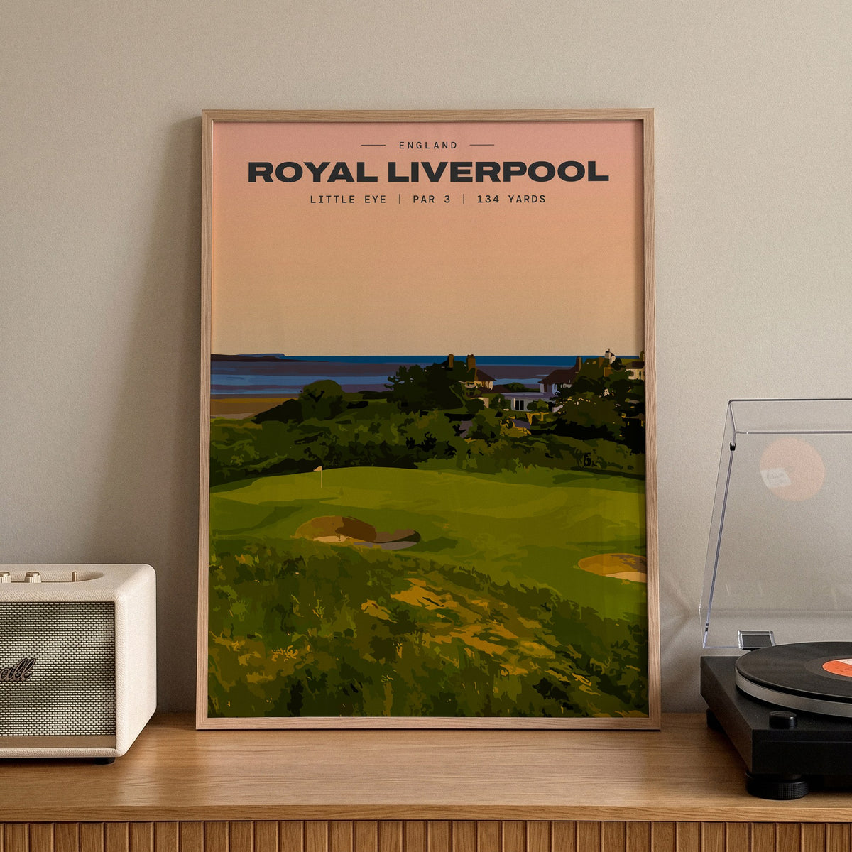 Royal Liverpool Little Eye golf print of a raised par 3 green at sunset, framed on a sideboard beside a record player