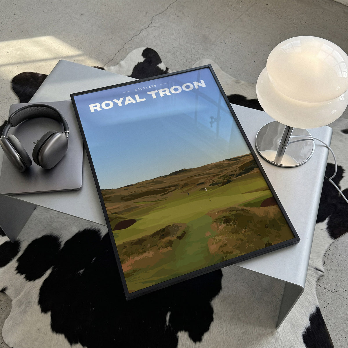 Royal Troon golf print of a links fairway through dunes to a flag, framed, lying on a steel table on a cowhide rug