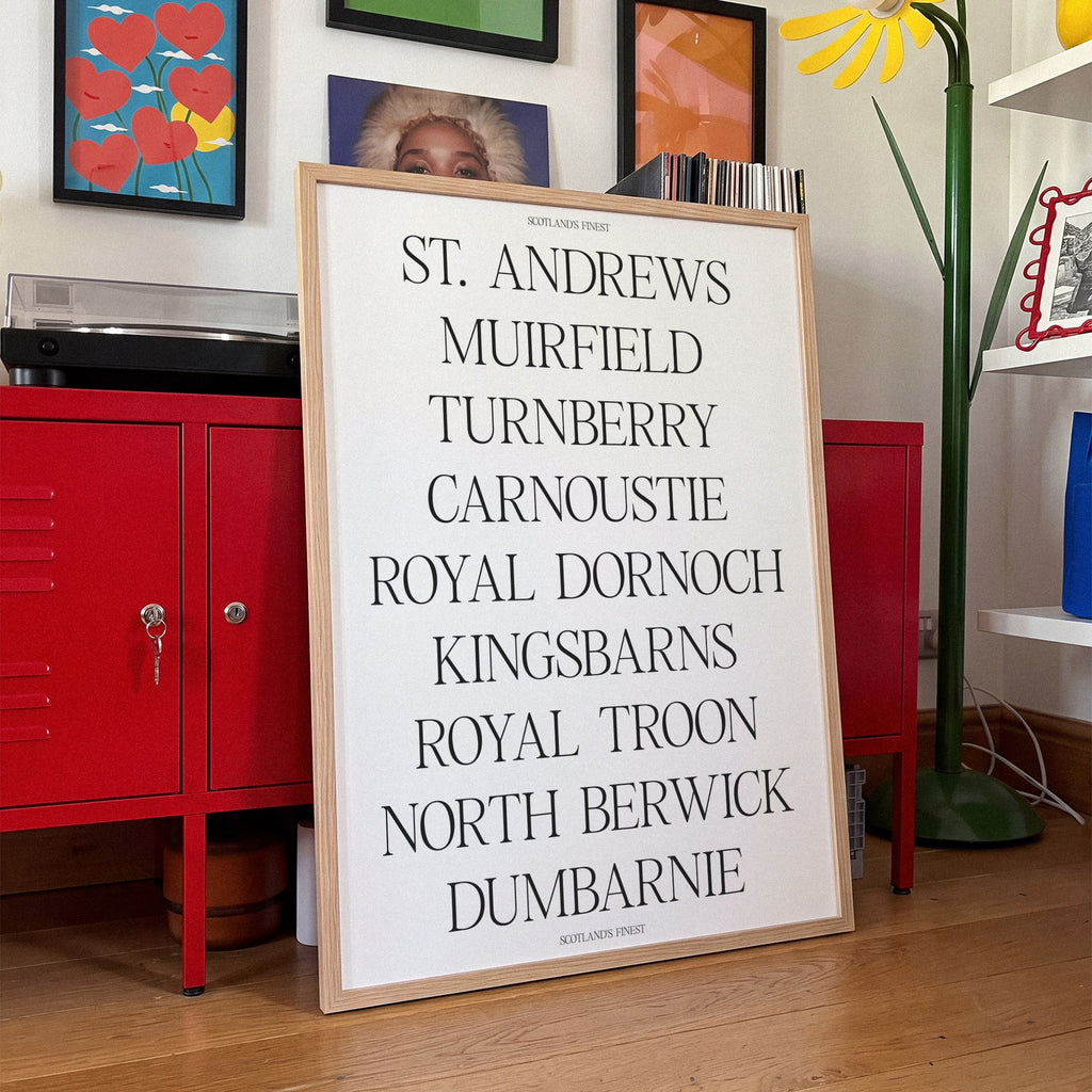 Scotland's Finest golf print of nine Scottish course names in serif type, framed, leaning against red lockers