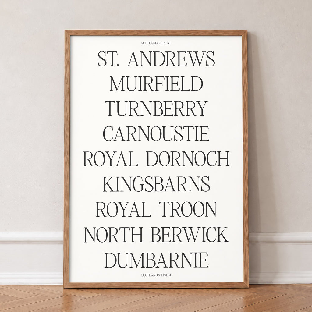 Scotland's Finest golf print of nine Scottish course names in serif type, in an oak frame, leaning against a wall on a herringbone floor