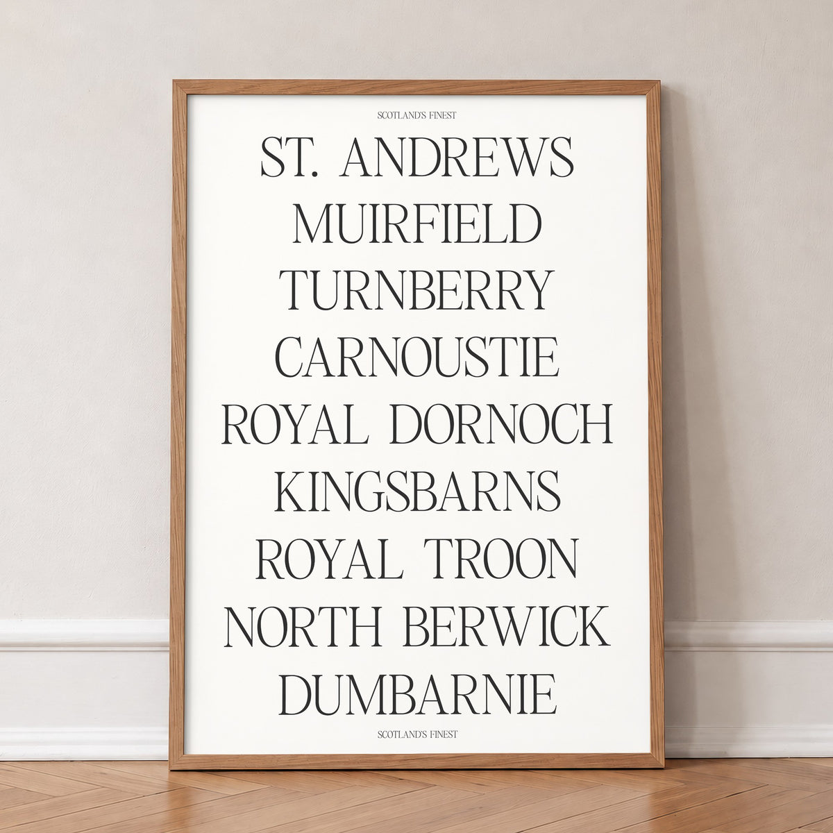 Scotland's Finest golf print of nine Scottish course names in serif type, in an oak frame, leaning against a wall on a herringbone floor