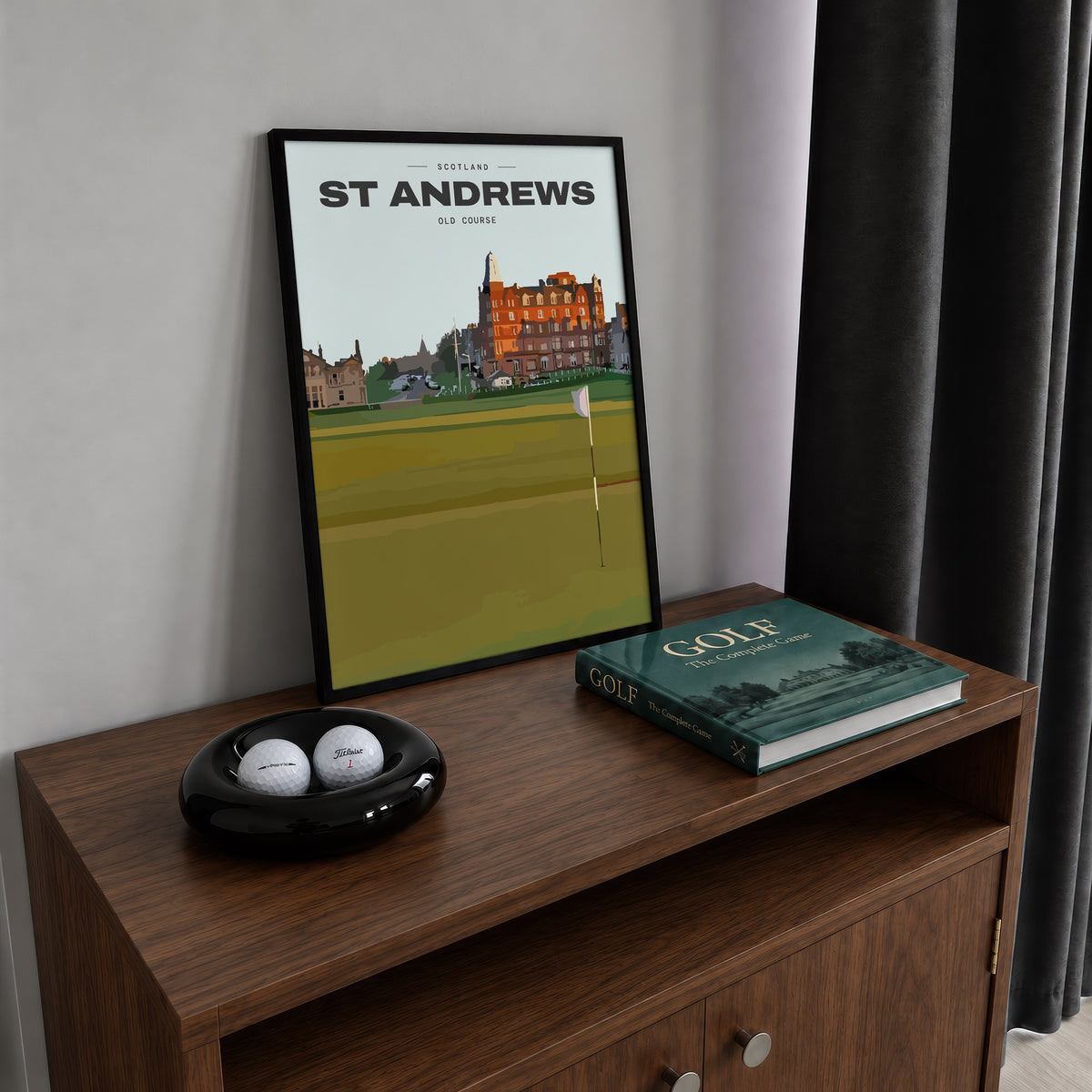 St Andrews Old Course golf print of the 18th green and flag below the town, framed on a walnut cabinet beside golf balls and a golf book