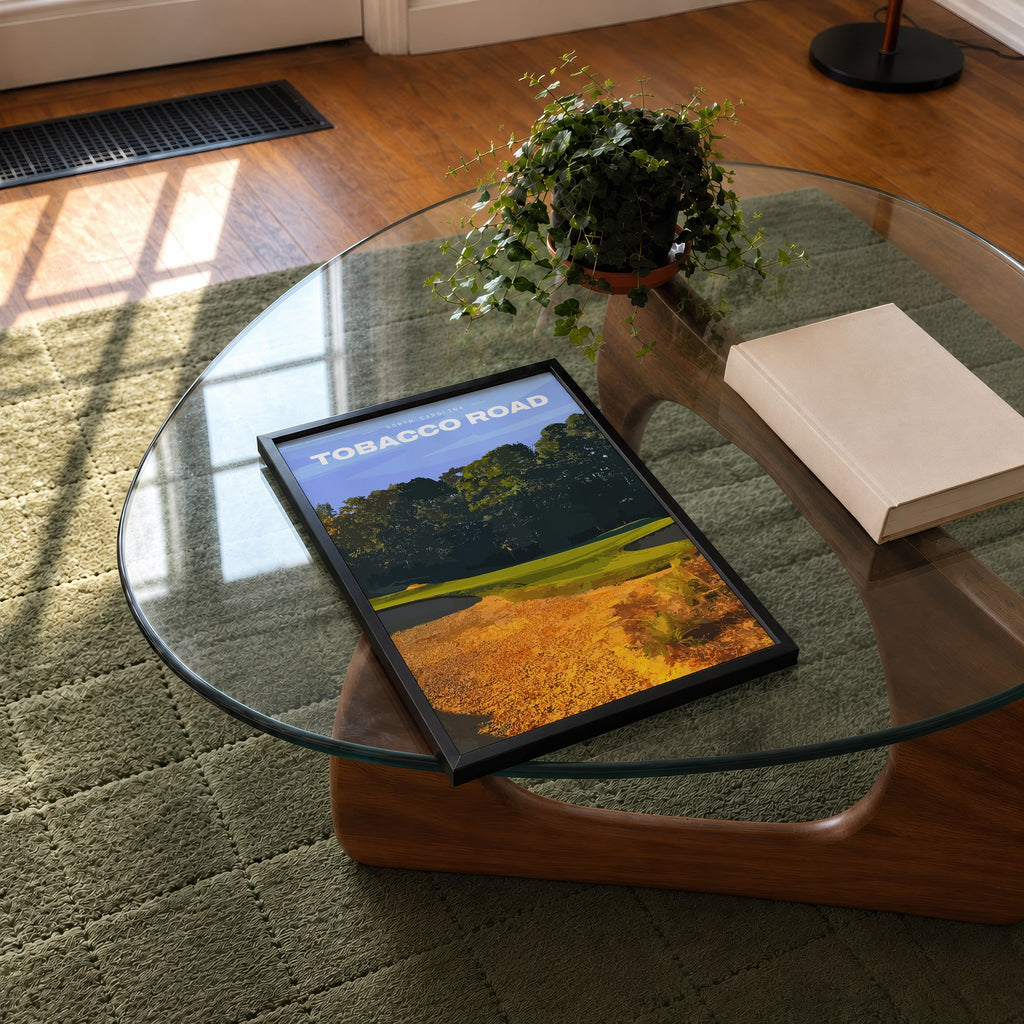 Tobacco Road golf print of a green behind golden sand and pines, framed on a glass coffee table