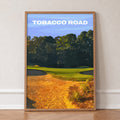 Tobacco Road golf print of a green behind golden sand and pines, in an oak frame, leaning against a wall on a herringbone floor