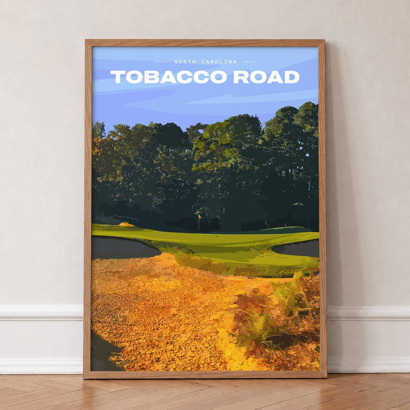 Tobacco Road golf print of a green behind golden sand and pines, in an oak frame, leaning against a wall on a herringbone floor