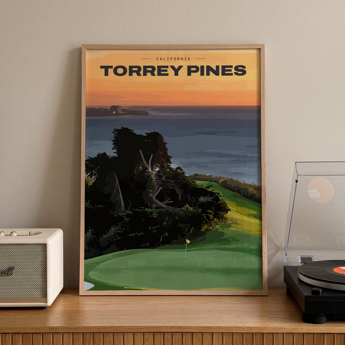 Torrey Pines golf print of a clifftop green above the Pacific at sunset, framed on a sideboard beside a record player