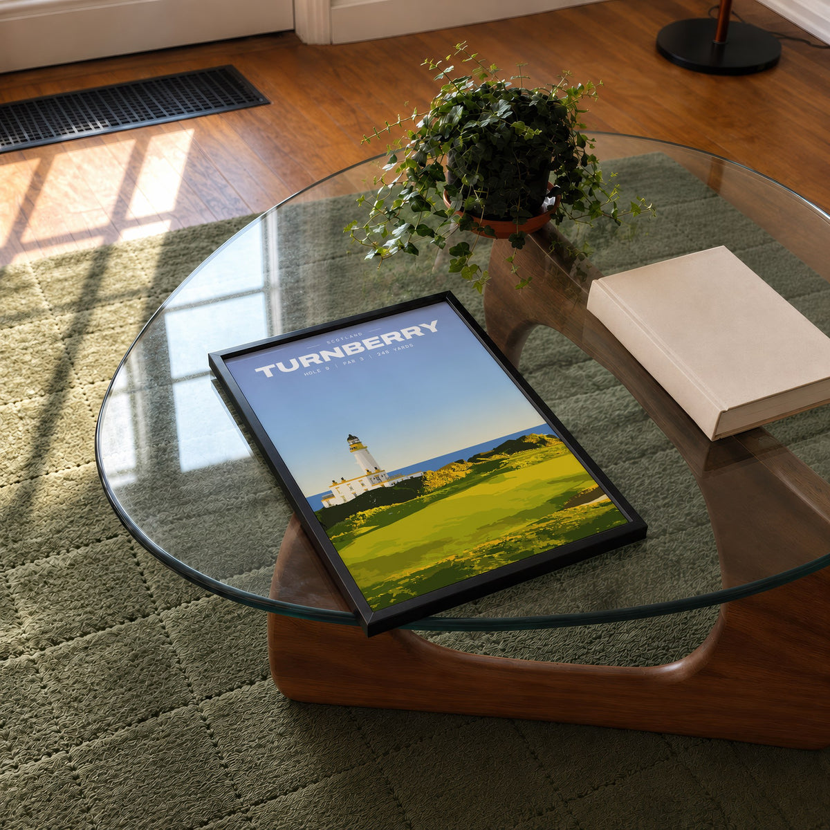 Turnberry 9th hole golf print of a white lighthouse above a links green, framed on a glass coffee table