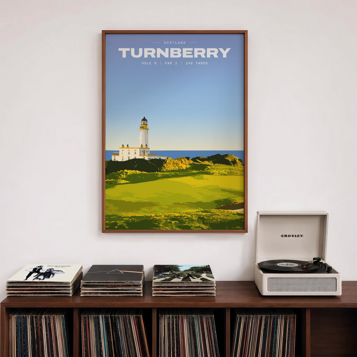 Turnberry 9th hole golf print of a white lighthouse above a links green, framed above a record shelf beside a turntable
