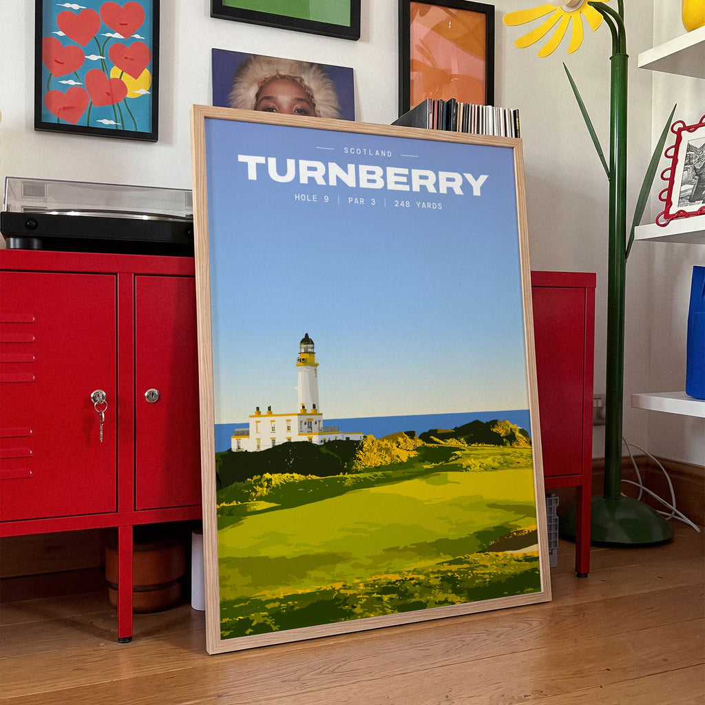 Turnberry 9th hole golf print of a white lighthouse above a links green, framed, leaning against red lockers