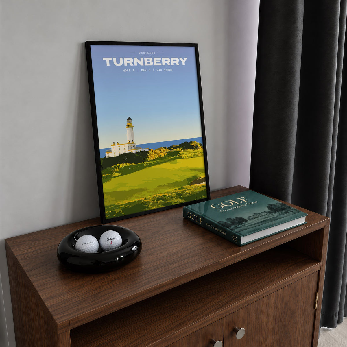 Turnberry 9th hole golf print of a white lighthouse above a links green, framed on a walnut cabinet beside golf balls and a golf book